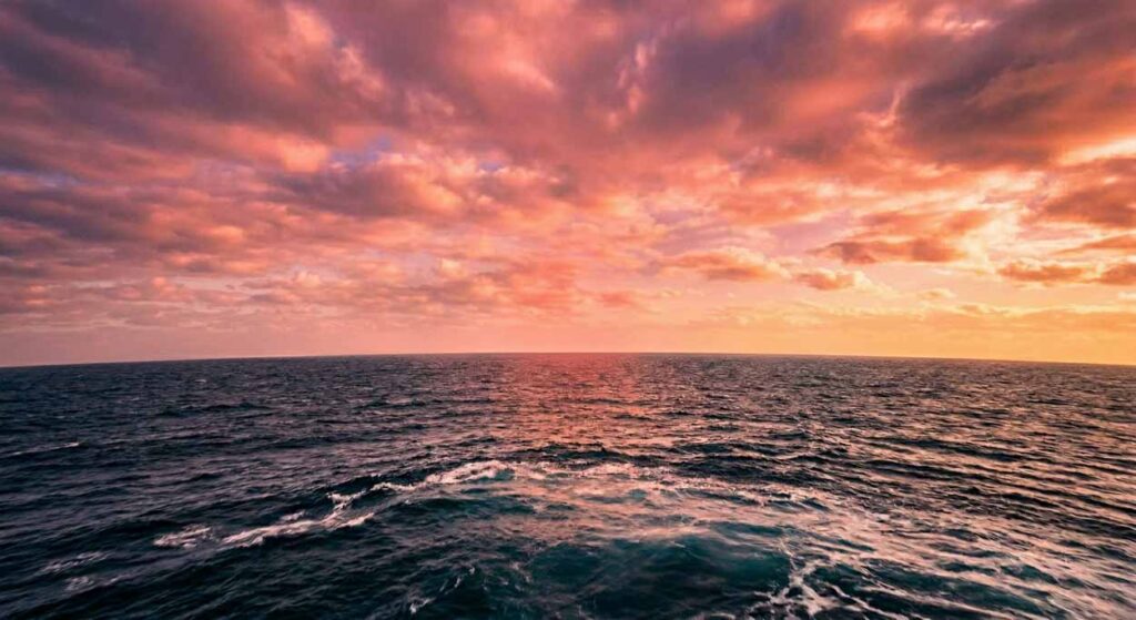 Šíry oceán počas sýto oranžového a ružového západu slnka, kde čistá línia horizontu prirodzene dokumentuje zakrivenie zemegule bez rušivých elementov.
