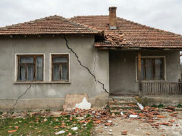 Fotorealistický záber na starší rodinný dom so šikmou prasklinou na sivej fasáde po zemetrasení 21. februára 2026. Ide o ilustračné foto.